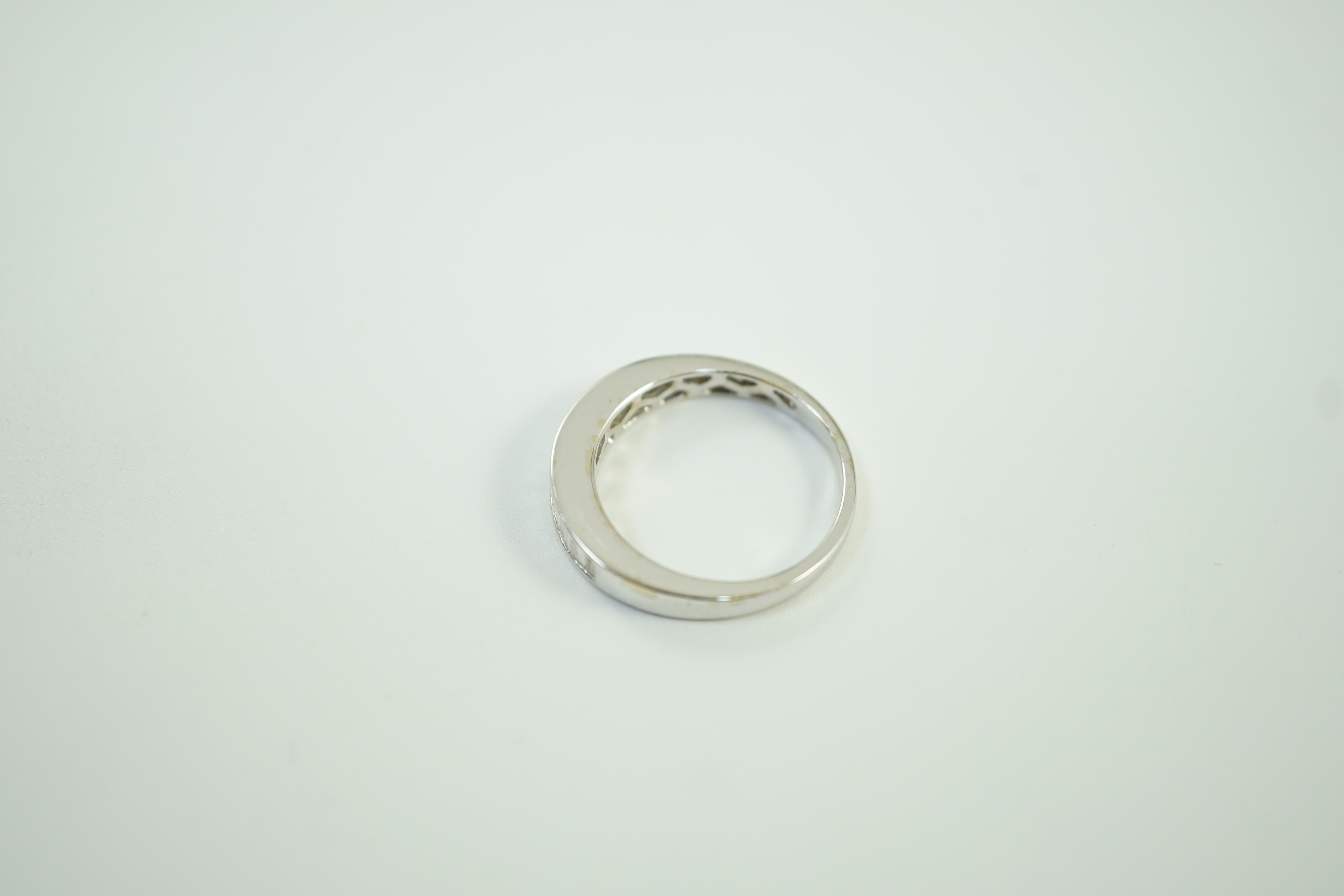 A modern white metal and graduated baguette cut channel set diamond half hoop ring, size M/N gross weight 3.7 grams.